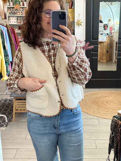 Détails soignés pour ce gilet sans manches en fausse fourrure écru sur la chemise, avec poches et surpiqûres camel. Un incontournable du dressing, à retrouver chez Abana, concept store au Pays Basque