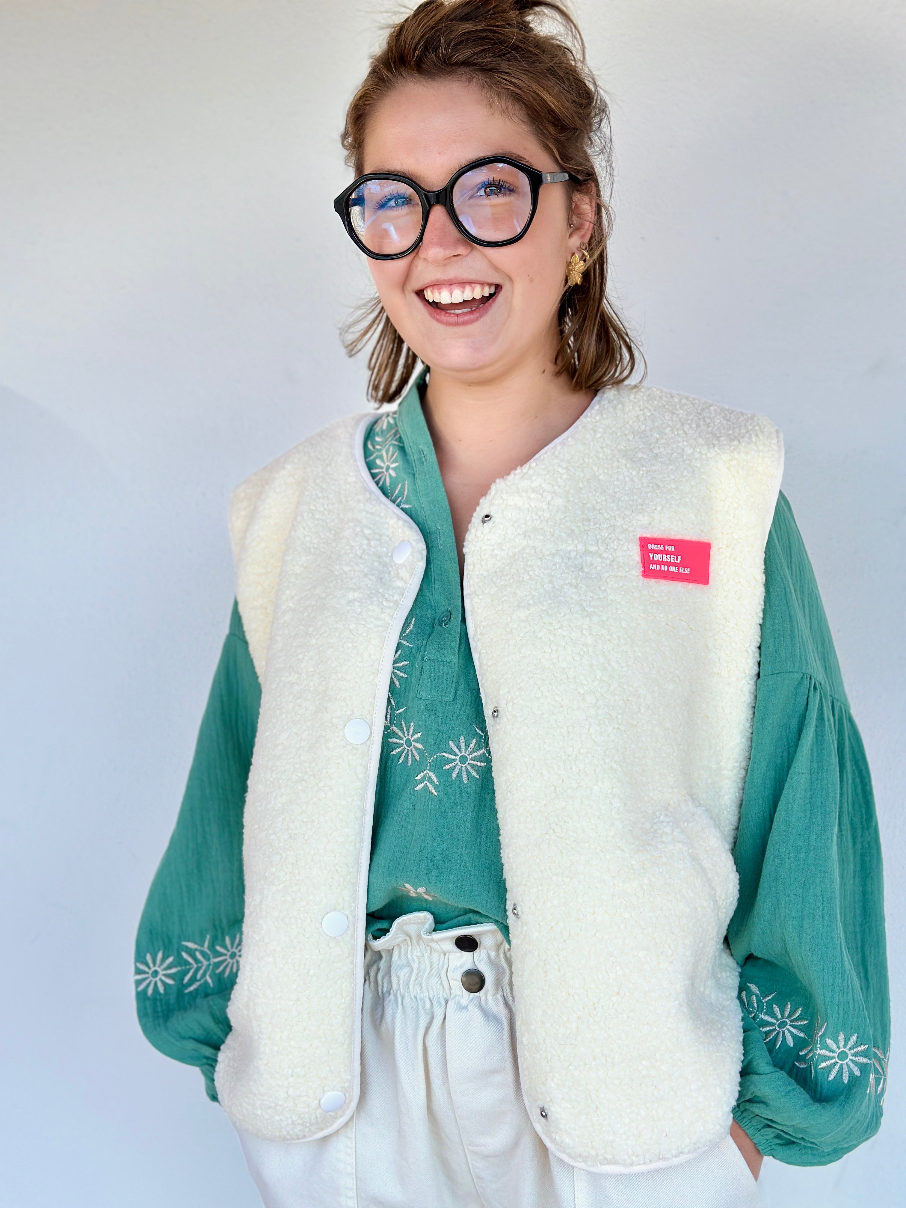 Gilet sherpa écru sans manches, coupe droite, fermeture à pressions, porté sur une blouse verte – Boutique Abana Ustaritz