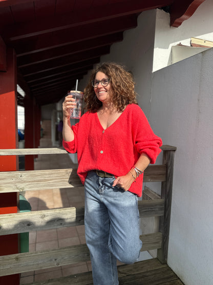 Pull rouge corail en maille douce, col V et boutons dorés, porté en look casual avec un jean - Abana Boutique 64480