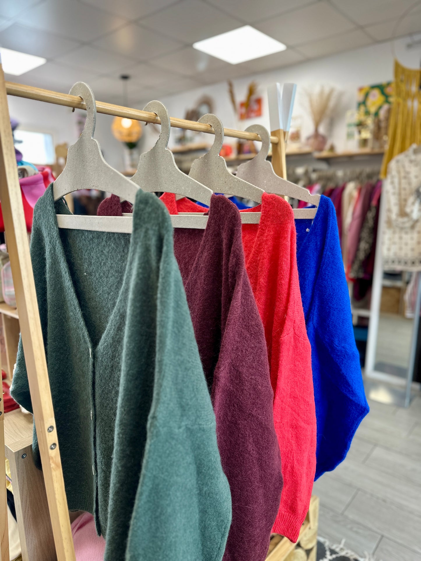 Collection de pulls doux colorés accrochés sur cintres : vert sapin, bordeaux, corail et bleu roi - Abana Boutique 64600