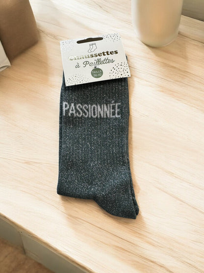 Chaussettes avec inscriptions humoristiques et pailletées, photographiées sur fond blanc doux, idéales pour un style décontracté et pétillant